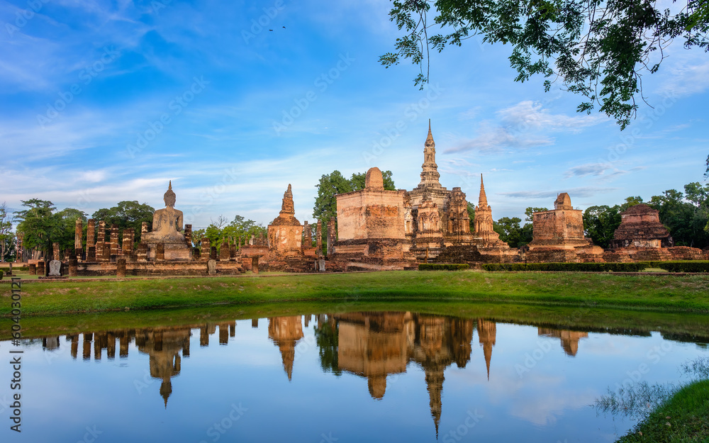 Beautiful wide view of ruins of 
Wat Mahathat Sukhothai at sun set with white clouds and blue sky on background. UNESCO and World Heritage Site. Travel  Concept.