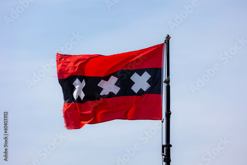 Photography Official flag of Amsterdam waving on the air in a sunny day and blue sky background, The flag depicts three Saint Andrew's Crosses and is based on the escutcheon in the coat of arms of Amsterdam