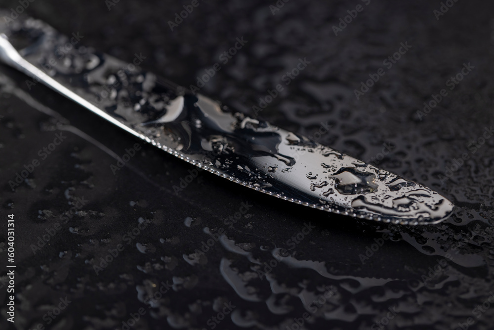 Fototapeta premium a steel knife covered with water droplets on black paper