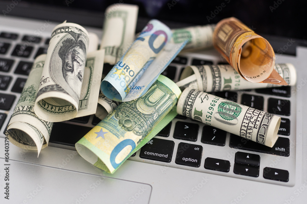 Fototapeta premium Make money online or online income concept. Roll of Dollar banknotes on laptop computer.