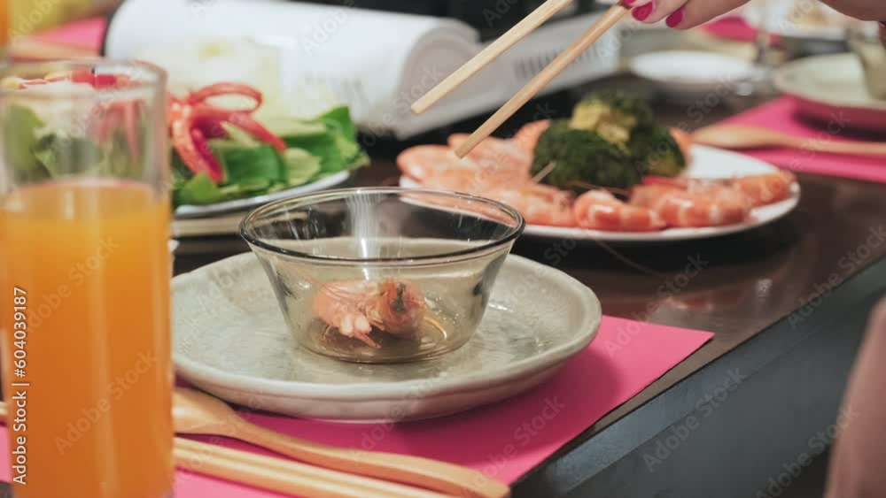 Close-up shot of hands of woman eating shrimps with wooden chopsticks while having holiday dinner on Tet