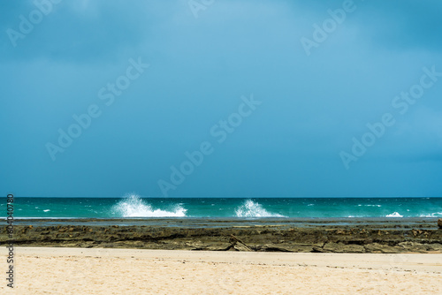 Layers of rainy sky  blue ocean  rocky barrier and white sand in brazilian beach