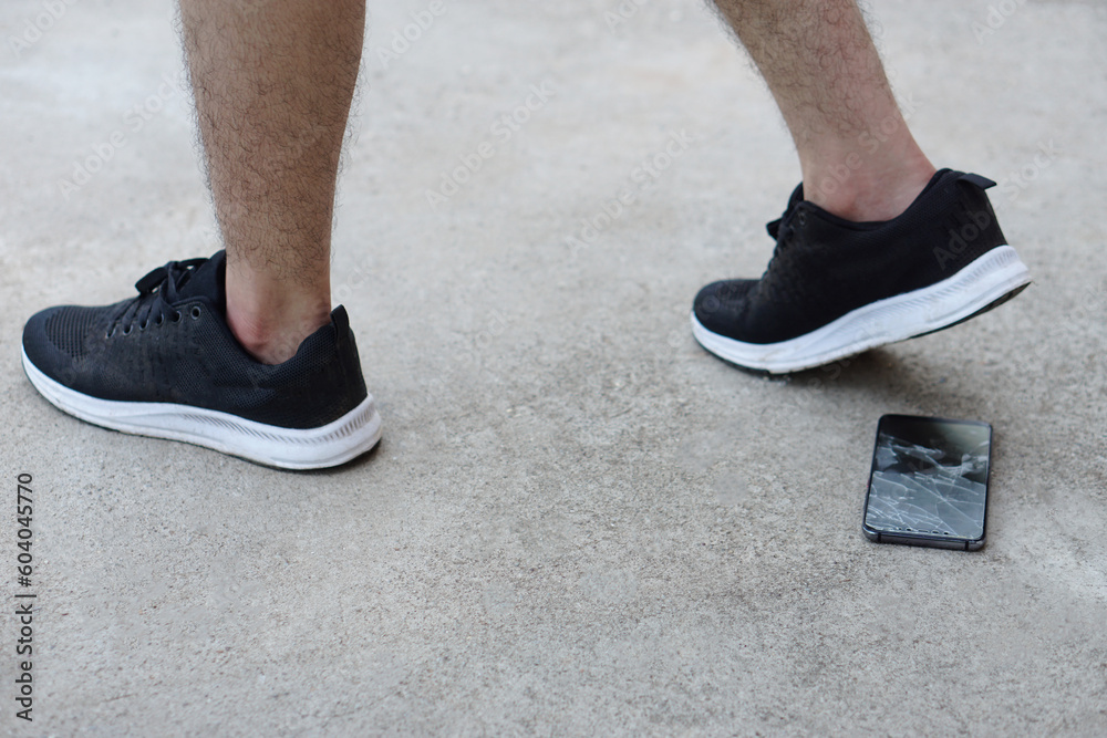 Closeup man wears black sport shoes, walking and his smartphone fell and broke on ground. Concept, damage with things in daily life from accident or careless. Mobile phone warranty claim for broken.