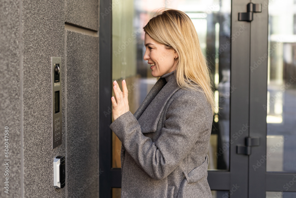 Happy woman ringing on doorbell at building entrance. Using intercom