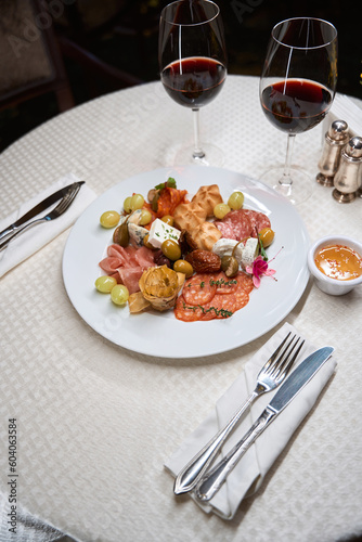 Plate with different snacks and red wine on white table in the restaurant