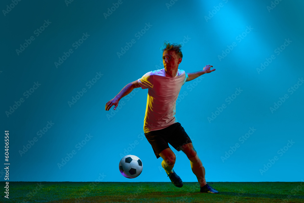 One energetic guy, sportsman, soccer player wearing black and white uniform training on football field in neon light. Concept of action, energy, sport