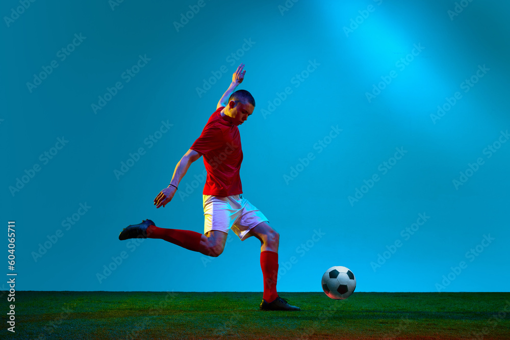 One sportsman, soccer player wearing red and white uniform training on football field in neon light. Concept of action, energy, sport, team game. Soccer workout