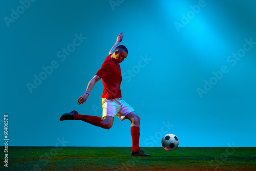 One sportsman, soccer player wearing red and white uniform training on football field in neon light. Concept of action, energy, sport, team game. Soccer workout