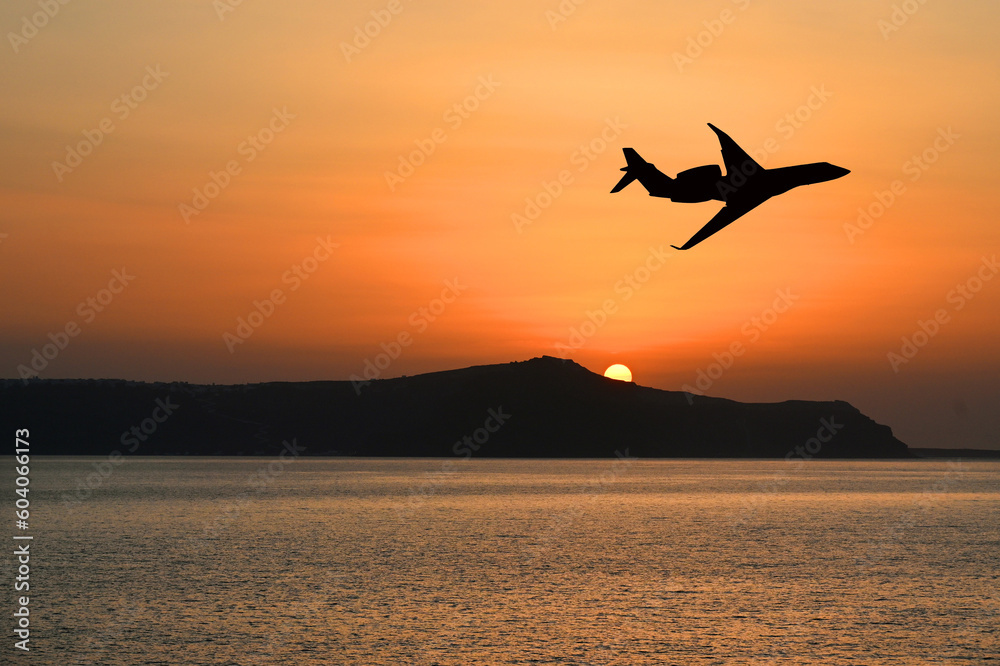 Silhouette of a private executive jet flying over an island at sunset. Luxury travel concept. Copy space. No people. - obrazy, fototapety, plakaty 