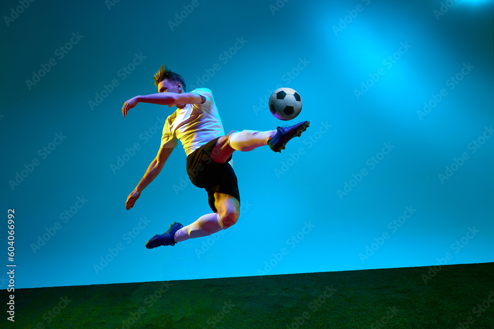 One sportsman, soccer player wearing yellow and black uniform hitting the ball in the air over football field in neon light. Concept of action, energy, sport One sportsman, soccer player wearing yellow and black uniform hitting the ball in the air over football field in neon light. Concept of action, energy, sport