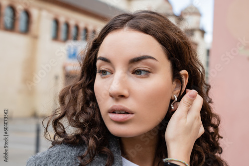 Photography Portrait of young and curly brunette woman touching hair and looking away while