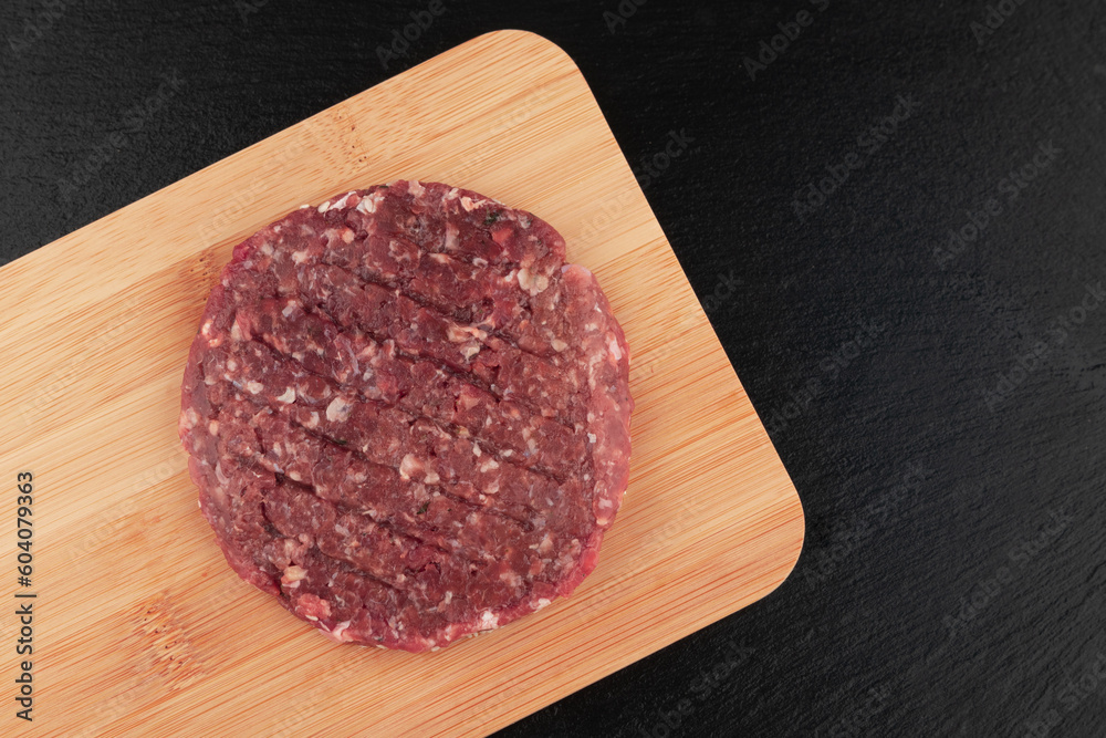 Raw hamburger patties on wooden cutting board on black background Raw hamburger patties on wooden cutting board on black background