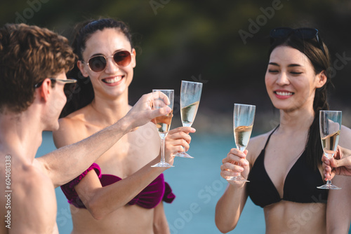 Man and woman friends group enjoy celebration party and fun luxury summer outdoor lifestyle by drinking champagne together, travel vacation on catamaran yacht boat sailing in tropical sea sunset on © chokniti