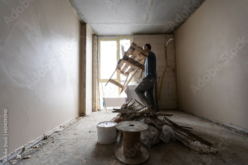 Construction worker wearing worker overall with wall plastering tools renovating apartment house. Plasterer renovating indoor walls and ceilings with float and plaster. Construction finishing works.