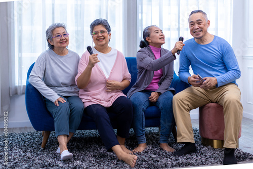 Happy senior Asian friends singing karaoke on the sofa in the living room with happy smiling face. Elderly people singing karaoke. Friends singing karaoke at home