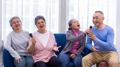 Happy senior Asian friends singing karaoke on the sofa in the living room with happy smiling face. Elderly people singing karaoke. Friends singing karaoke at home