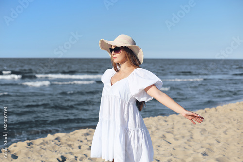 Happy blonde woman is on the ocean beach in a white dress and sunglasses, open arms.