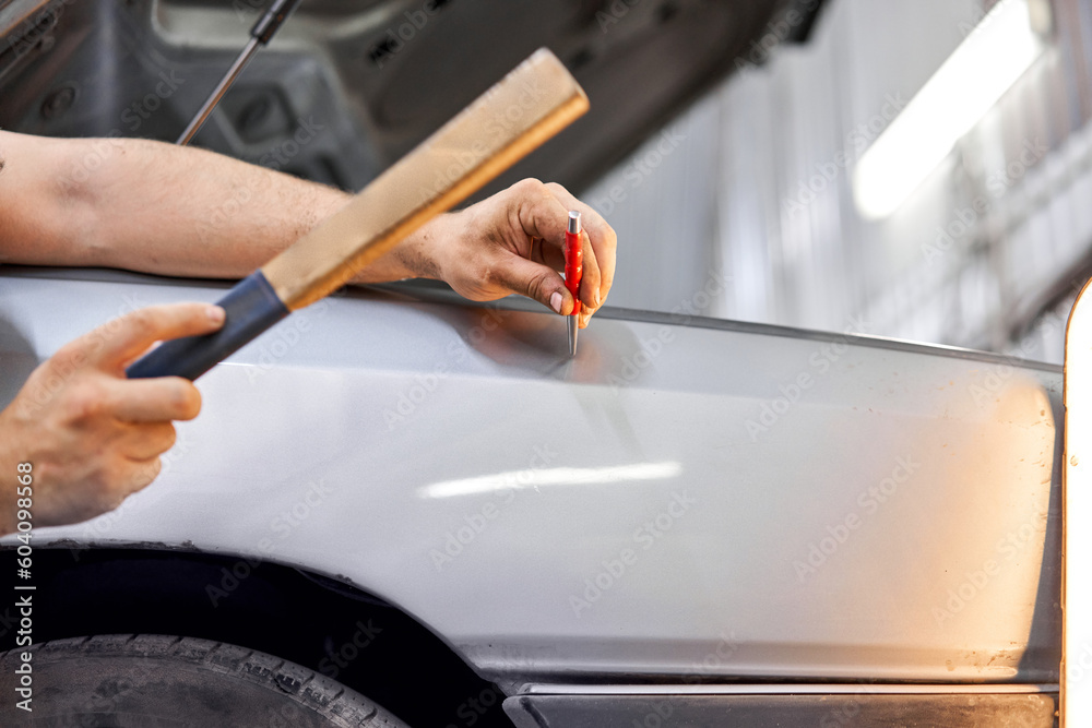 A car service worker knocks with a hammer. Removing dents on the car. PDR technology. Car body repair without painting.