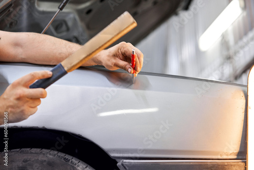 A car service worker knocks with a hammer. Removing dents on the car. PDR technology. Car body repair without painting.