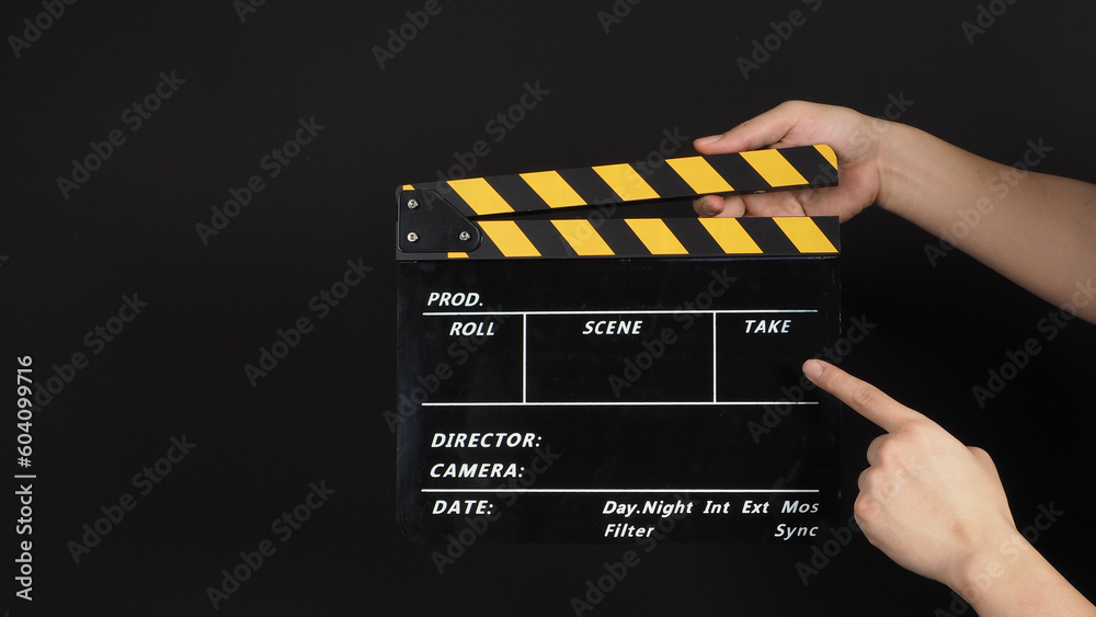 Naklejka premium Hand's holding and point at yellow and black Clapper board on black background.