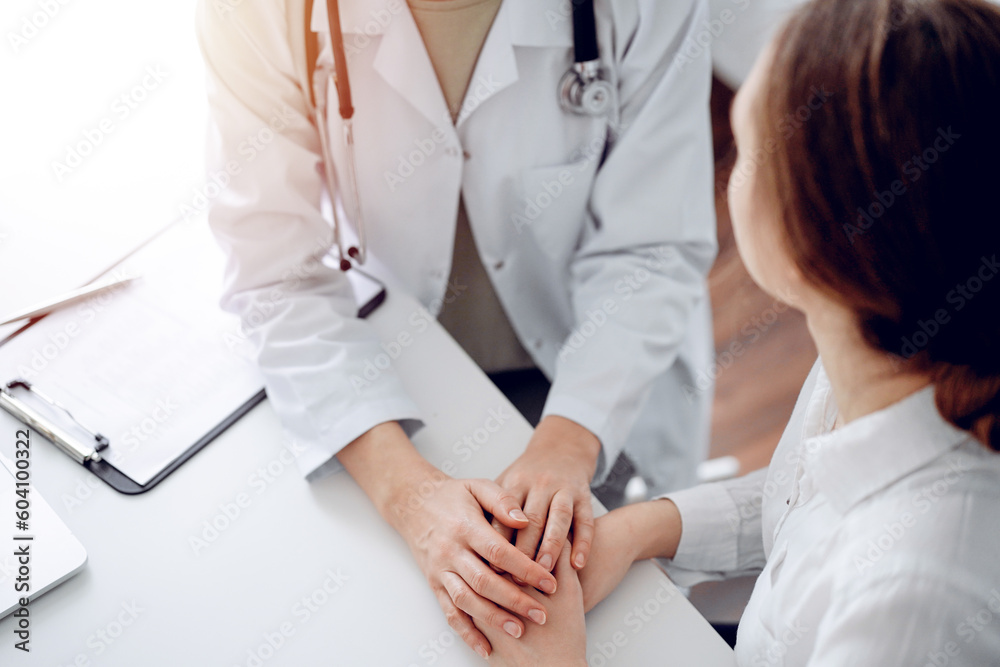 Doctor and patient sitting at the desk in clinic office. The focus is on female physician's hands reassuring woman, close up. Perfect medical service, empathy, and medicine concept. Doctor and patient sitting at the desk in clinic office. The focus is on female physician's hands reassuring woman, close up. Perfect medical service, empathy, and medicine concept.