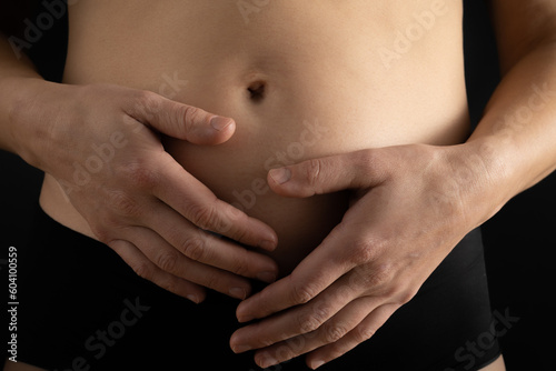 Very close up view of pregnant woman holding her belly gently during first months of pregnancy. Pregnancy first trimester - week 18. Close up. Front view. Black background. Bright shot.