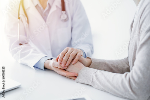 Doctor and patient sitting at the table in clinic office. The focus is on female physician's hands reassuring woman, only hands close up. Medicine concept. © rogerphoto