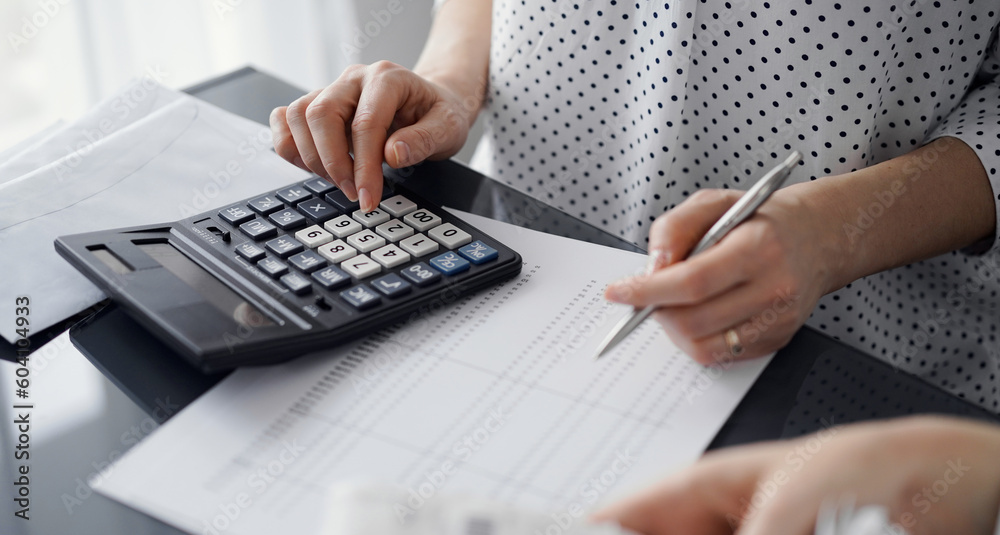 Woman accountant using a calculator and laptop computer while counting taxes for a client. Business audit and finance concepts. Woman accountant using a calculator and laptop computer while counting taxes for a client. Business audit and finance concepts.