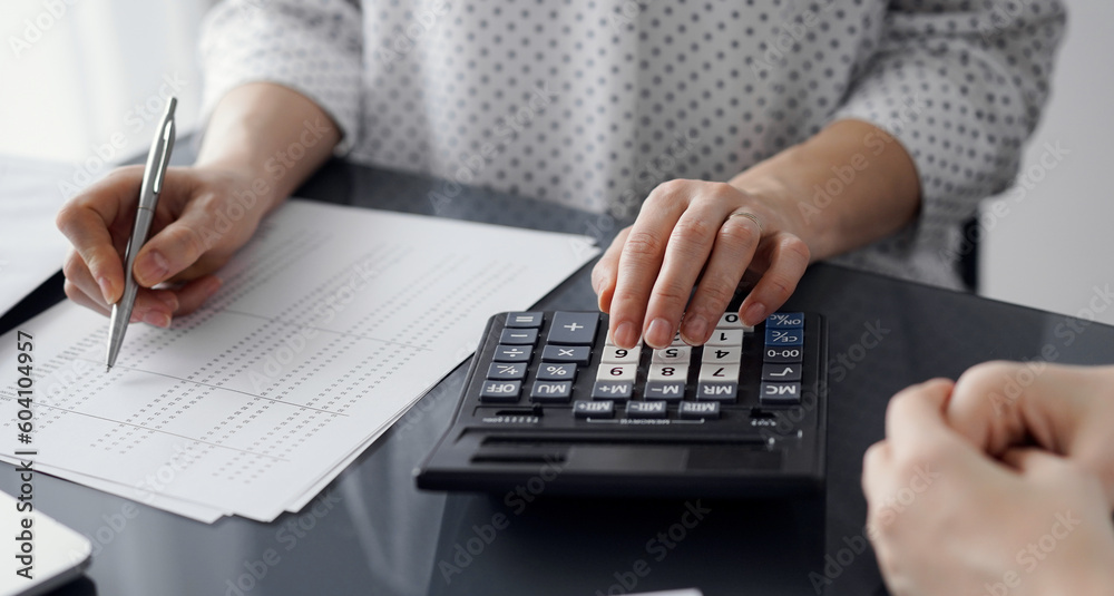 Woman accountant using a calculator and laptop computer while counting taxes for a client. Business audit and finance concepts. Woman accountant using a calculator and laptop computer while counting taxes for a client. Business audit and finance concepts.