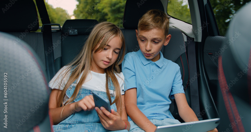 Children boy and girl sit in car using digital tablet for games and entertainment, celebrate vin and give high fives traveling by car. Concept of a family holiday.