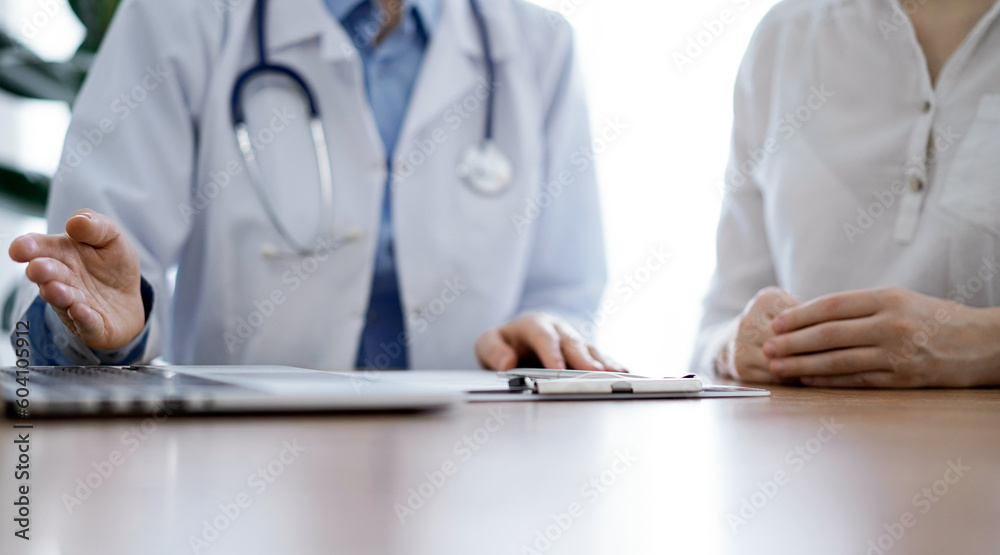 Doctor and patient discussing something while using laptop computer and sitting near each other at the wooden desk in clinic. Medicine concept. Doctor and patient discussing something while using laptop computer and sitting near each other at the wooden desk in clinic. Medicine concept.