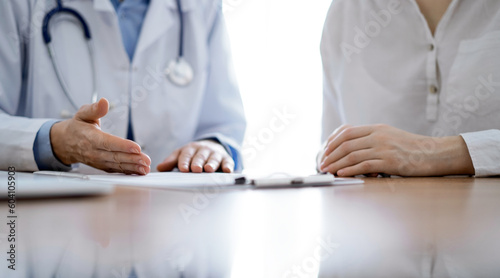 Doctor and patient discussing something while sitting near each other at the wooden desk in clinic. Medicine concept.