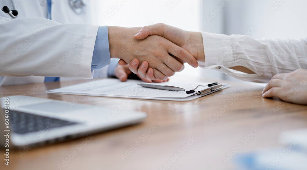 Doctor and patient shaking hands above the wooden table in clinic. Medicine concept. Doctor and patient shaking hands above the wooden table in clinic. Medicine concept.