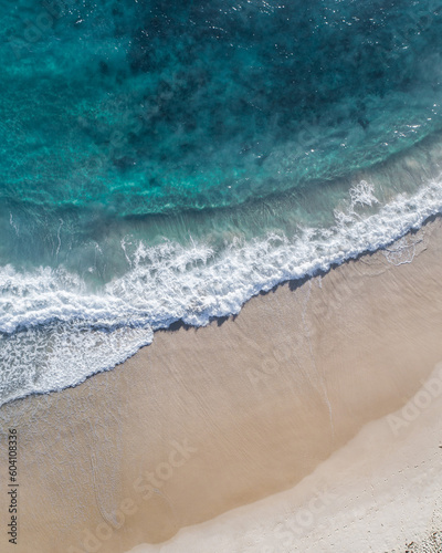 Drone view of an idyllic ocean with gentle waves near a stunning sand beach at a holiday resort