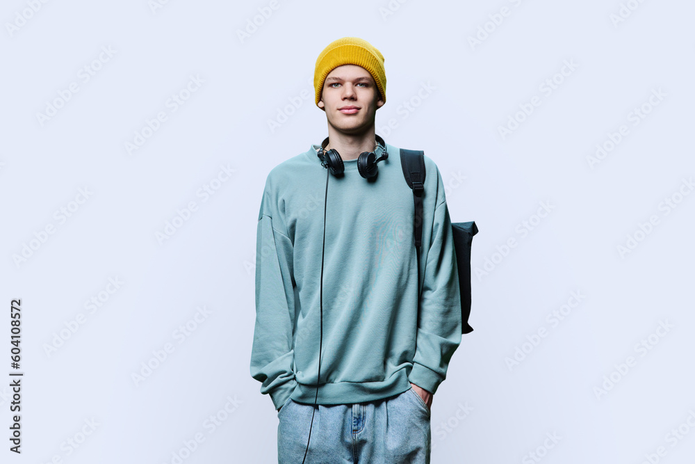 Young male in yellow cap sweatshirt with headphones backpack on white background
