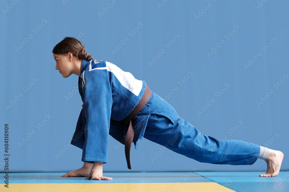Judo girl with brown belt. A judoka teenager fighter poses in a blue kimono on a plain background. Japanese martial art. The process of martial arts training. Healthy lifestyle, sports concept
