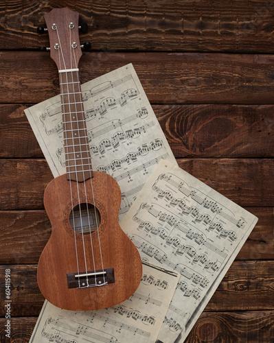 Ukulele guitar on music sheets on wooden background