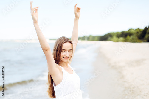Happy smiling woman in free happiness bliss on ocean beach standing with raising hands. Portrait of a multicultural female model in white summer dress enjoying nature during travel holidays vacation o © rogerphoto
