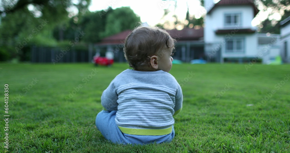Cute baby infant in outdoor home grass. Residential home in background with toddler in foreground Cute baby infant in outdoor home grass. Residential home in background with toddler in foreground