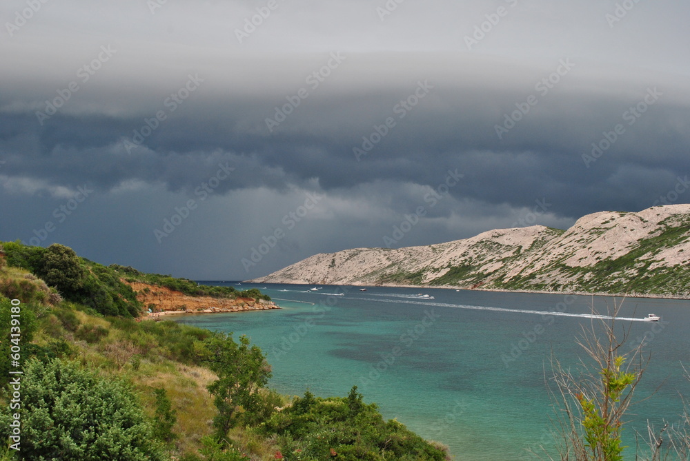 Storm arriving in the distance in the bay of the island of Rab. Wind that increases and boats returning to port at high speed. Contrast between the blue of the sea and the dark and gloomy sky.
