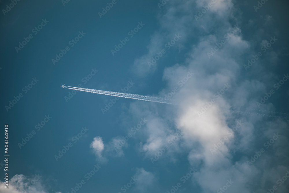 Blue sky with clouds from which a commercial airplane appears leaving a white trail Blue sky with clouds from which a commercial airplane appears leaving a white trail