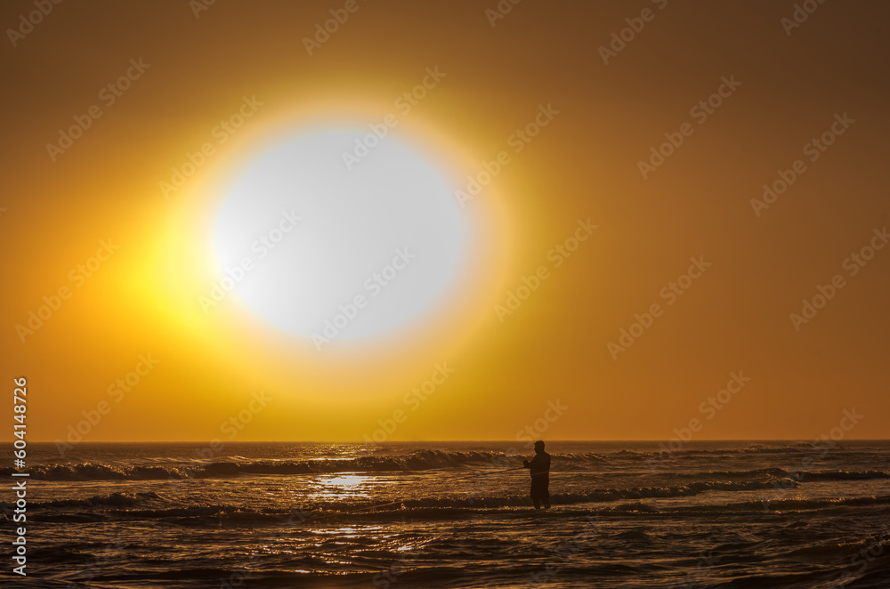 Man standing in the sea while fishing at sunset.