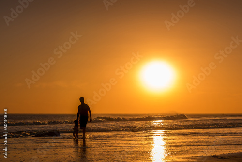 Man walking with a girl along the seashore on the beach at sunset.