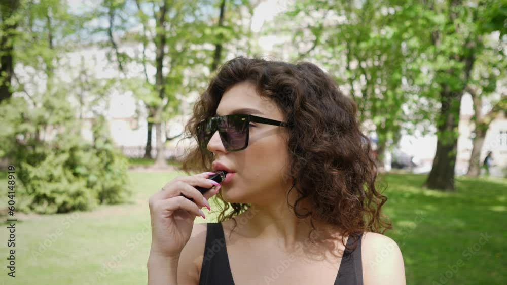 close portrait of a young woman who smokes an electronic cigarette in a city park 4k close portrait of a young woman who smokes an electronic cigarette in a city park 4k