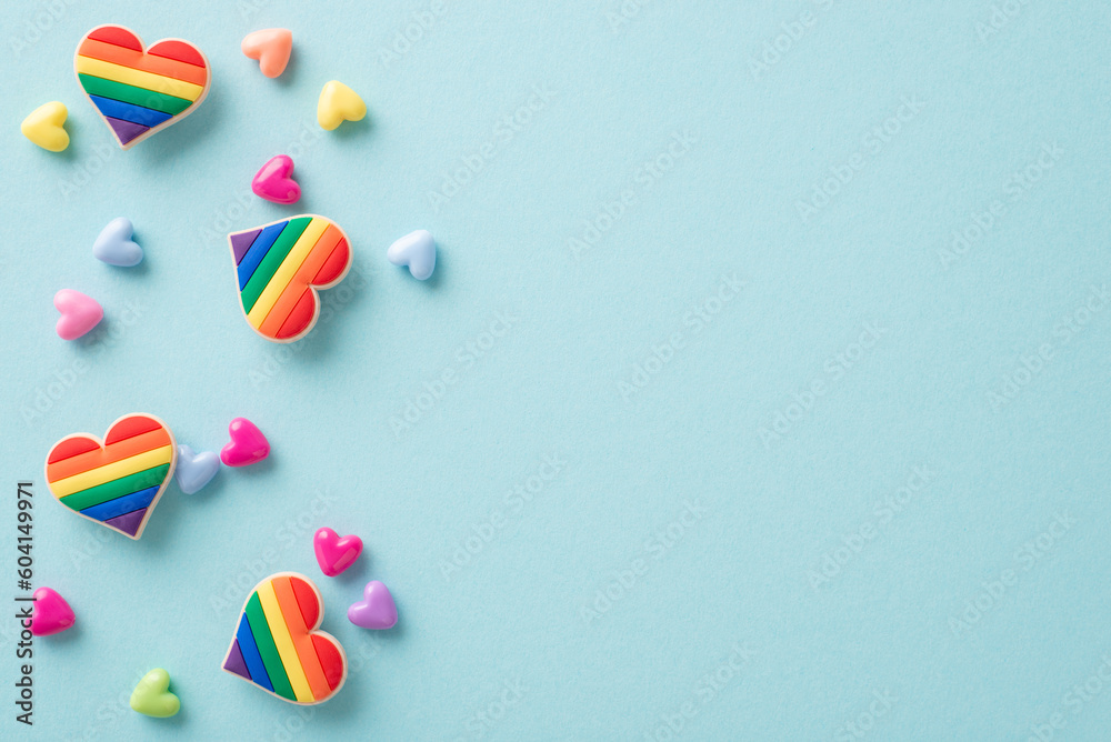 Symbolic LGBTQ+ accessories like rainbow-colored heart pins seen from above on a pastel blue background, with plenty of space for text or advert - obrazy, fototapety, plakaty 