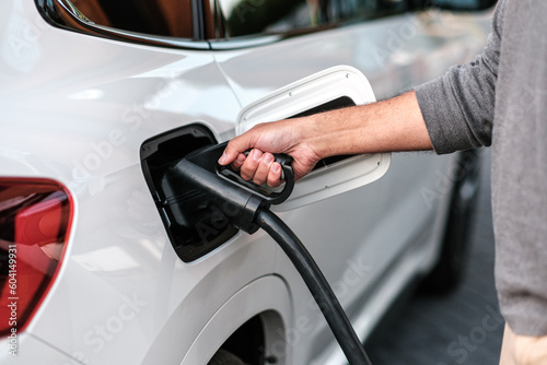 Man plugging in a CCS charger to a white car at a electric vehicle fast charging station, closeup. Renewable energy. The sustainable future of transportation. © Sidney vd Boogaard