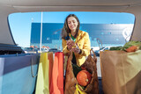 Woman in yellow jacket puts shopping bags with a groceries into a car trunk