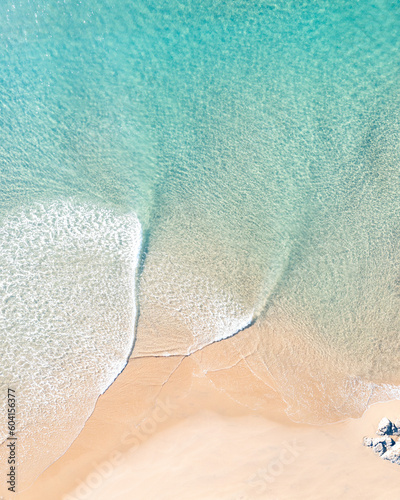 Drone view of an idyllic ocean with gentle waves near a stunning sand beach at a holiday resort
