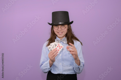 Beginning novice magician conjurer. Girl with cards in her hands in a hat with a top hat and a striped shirt with a bow tie