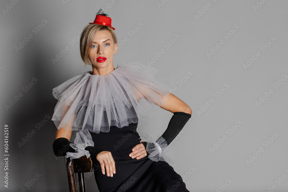 Elite clown. Woman dressed as clown iblack dress with harlequin collar and red hat. Contrast image on grey background. High quality photo